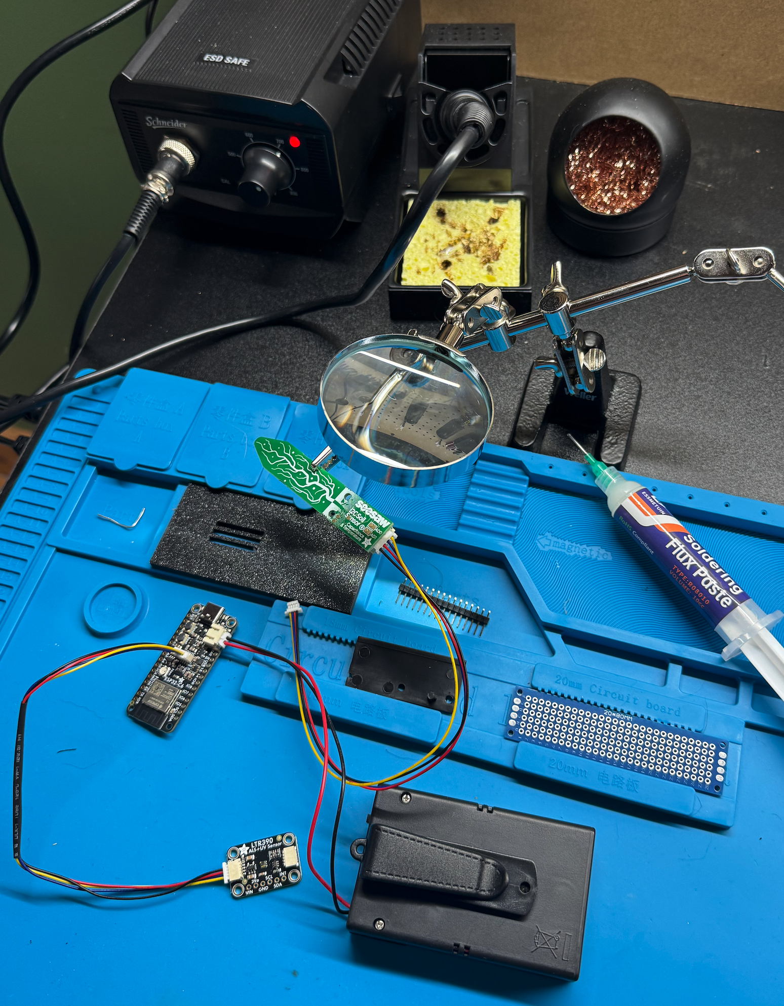 Askew Auk prototype on a soldering mat with helping hands, flux paste, and scattered components