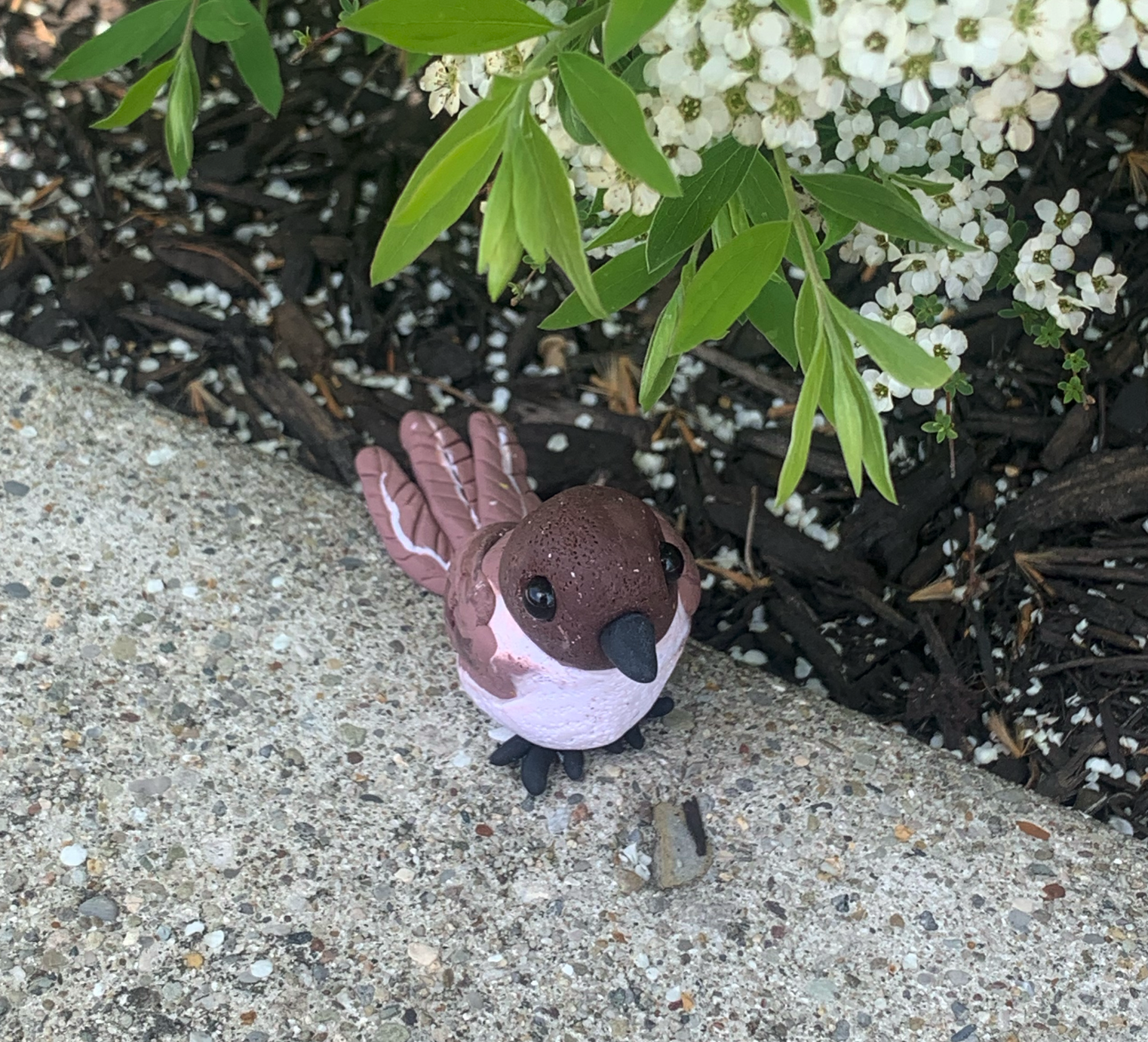 Clay Phoebe sculpture in a garden, front view, under white flowering branches